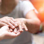 Doctor physician hand on happy elderly senior patient to comfort in hospital examination room or hospice nursing home or wellbeing county.