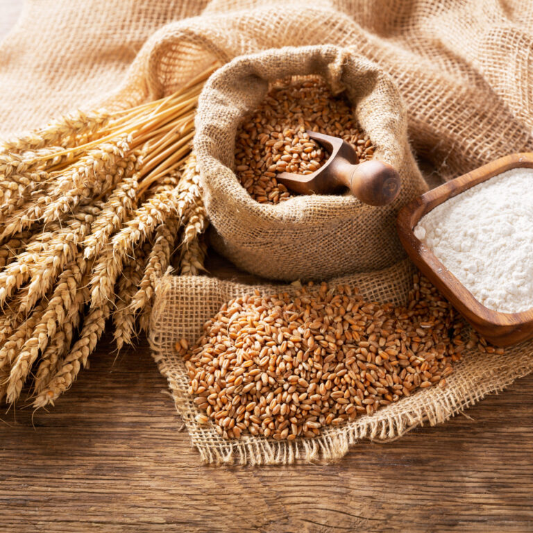 wheat ears, grains and bowl of flour on a wooden table, top view