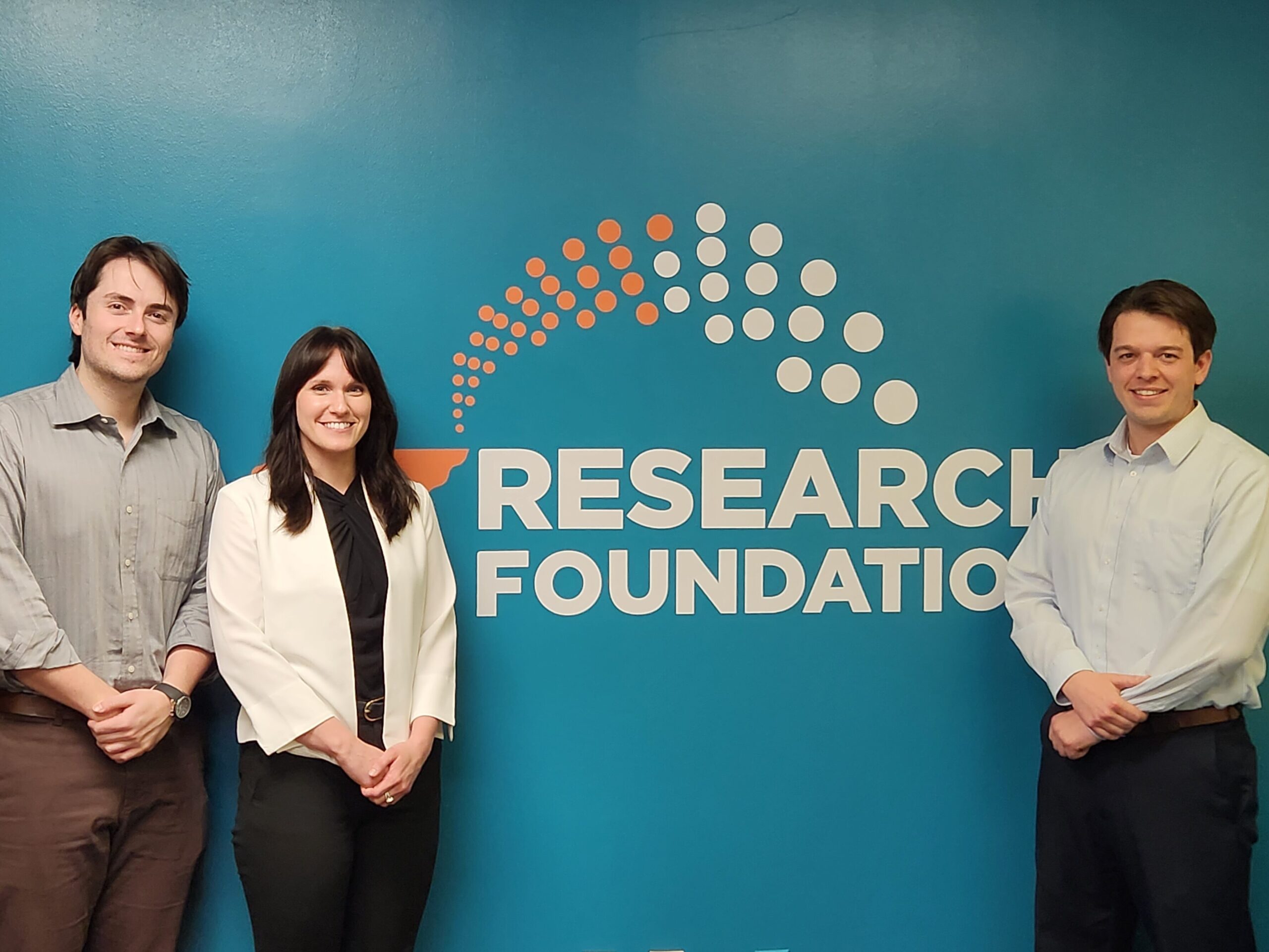 (Left to right) Jack Pitcock, Haley Rainwaiter and Maxwell Schwam stand for a photo in front of the UTRF logo wall.