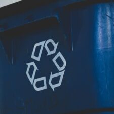 A white recycling symbol on the side of a blue plastic bin